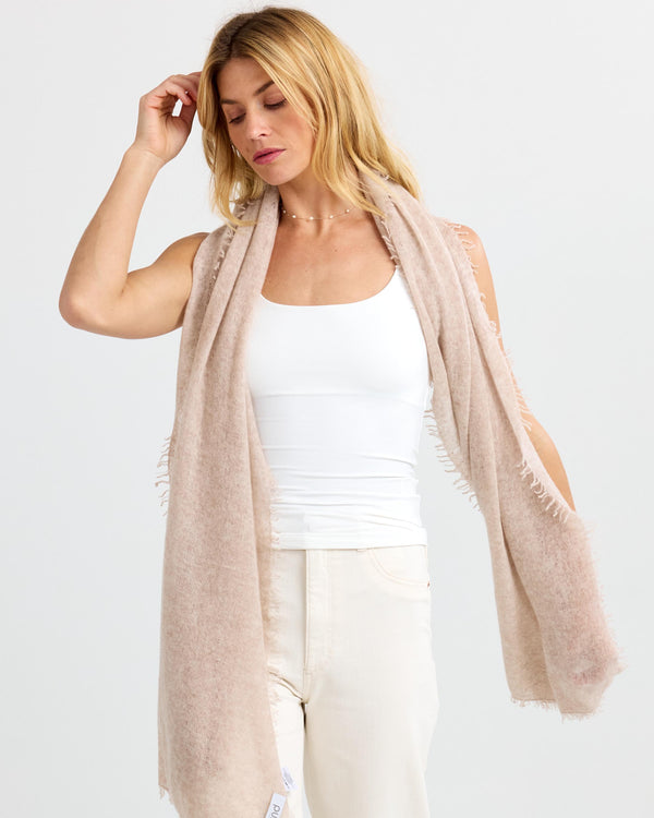 LIFESTYLE / EDITORIAL: Woman wearing beige cashmere scarf over white tank top and cream pants against plain background