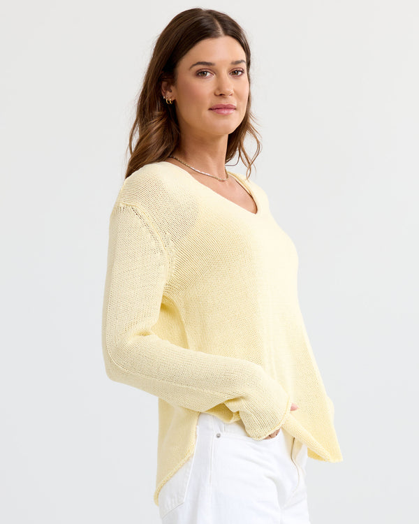 LIFESTYLE / EDITORIAL: Woman wearing a buttermilk yellow V-neck cashmere sweater and white pants, standing against a white