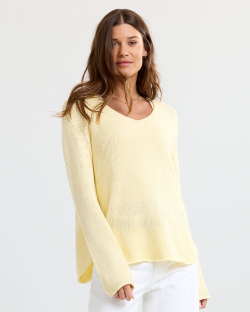 Woman wearing a light yellow V-neck cashmere sweater and white pants against a plain light background