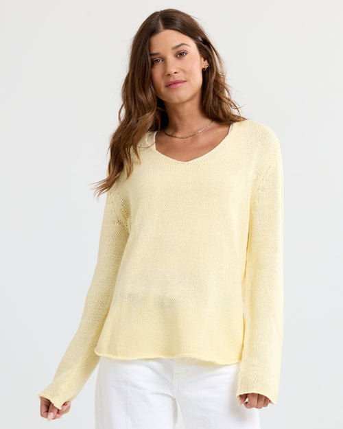 Front view image of a woman wearing a buttermilk yellow V-neck cashmere sweater and white pants standing