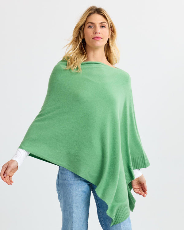 Woman wearing matcha green cashmere poncho over white long sleeves and blue jeans against plain background