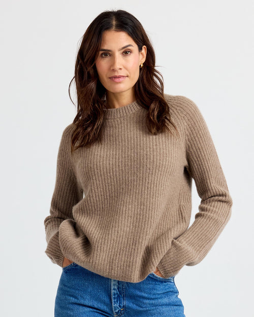 LIFESTYLE / EDITORIAL: Woman wearing a driftwood-colored ribbed cashmere sweater with blue jeans against a plain background