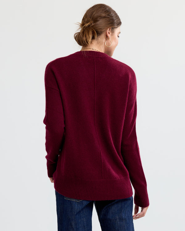 LIFESTYLE / EDITORIAL: Woman facing away wearing a cabernet red cashmere sweater and blue jeans against a plain background