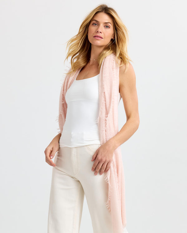 LIFESTYLE / EDITORIAL: Woman wearing light pink cashmere scarf, white tank top, and cream pants against plain background