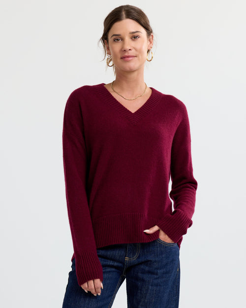 LIFESTYLE / EDITORIAL: Woman wearing a cabernet red V-neck cashmere sweater and blue jeans against a plain background