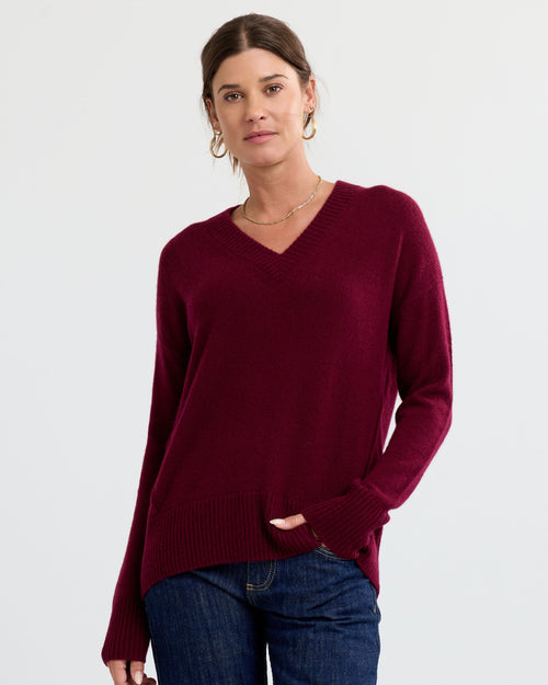 Front-facing image of a woman wearing a cabernet red V-neck cashmere sweater and blue jeans against white background