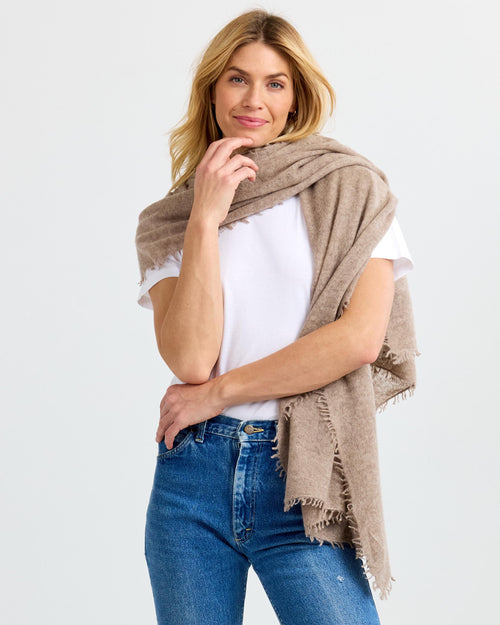 LIFESTYLE / EDITORIAL: Woman wearing beige cashmere shawl over white t-shirt and blue jeans, standing against white