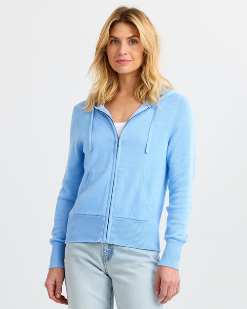 Front-facing image of a woman wearing a light blue zip-up cashmere hoodie with light wash jeans