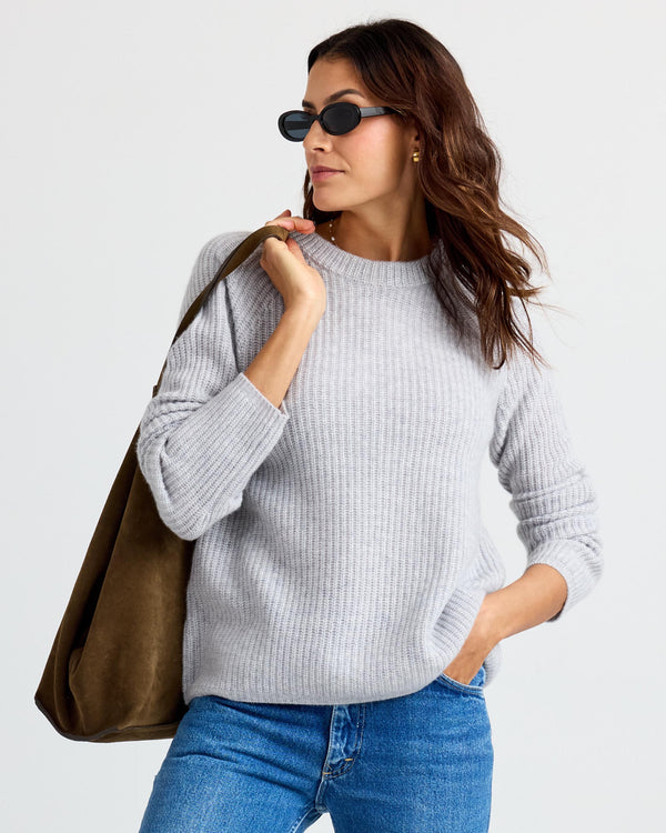 LIFESTYLE / EDITORIAL: Woman wearing gray ribbed cashmere sweater, blue jeans, sunglasses, and carrying large brown suede bag