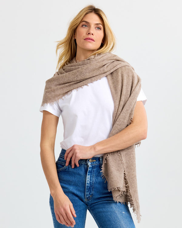 LIFESTYLE / EDITORIAL: Woman wearing beige cashmere shawl over white t-shirt and blue jeans against plain background