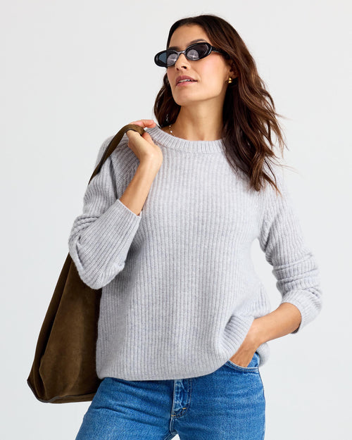 LIFESTYLE / EDITORIAL: Woman wearing gray ribbed cashmere sweater, blue jeans, sunglasses, and carrying a brown suede bag