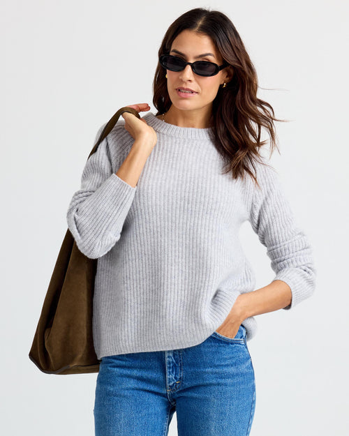 LIFESTYLE / EDITORIAL: Woman wearing light gray ribbed cashmere sweater, blue jeans, sunglasses, and carrying brown tote bag