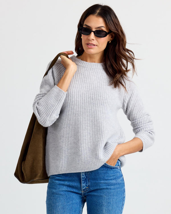 LIFESTYLE / EDITORIAL: Woman wearing light gray ribbed cashmere sweater, blue jeans, sunglasses, and carrying brown tote bag