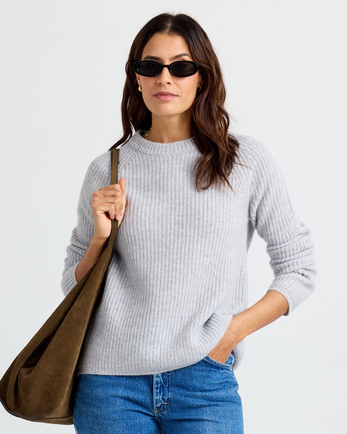LIFESTYLE / EDITORIAL: Woman wearing gray ribbed cashmere sweater, blue jeans, sunglasses, and carrying olive green bag