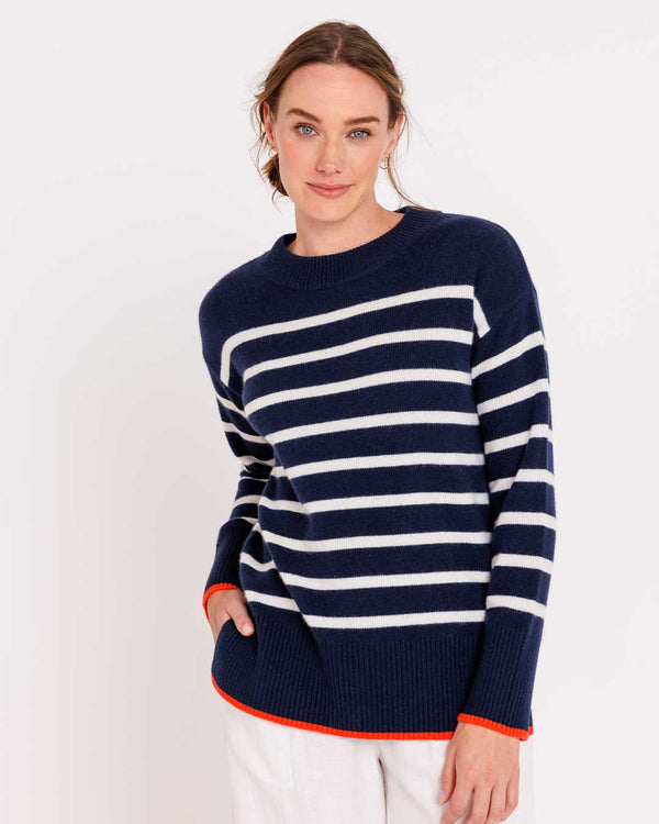 LIFESTYLE / EDITORIAL: Woman wearing navy and ivory striped cashmere sweater with orange trim, posing against white