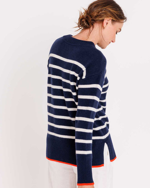 LIFESTYLE / EDITORIAL: Woman wearing navy and ivory striped cashmere sweater with orange trim, facing sideways against white
