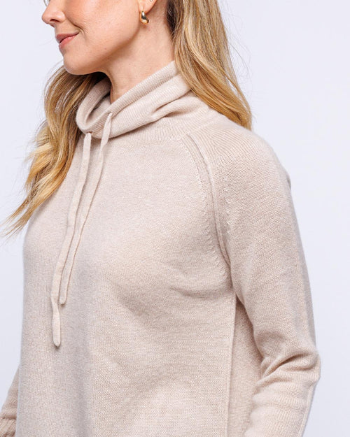 LIFESTYLE / EDITORIAL: Woman wearing oatmeal-colored cashmere drawstring funnel neck sweater, side profile view
