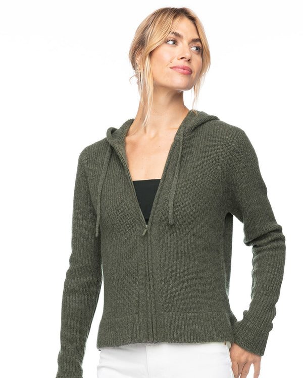 LIFESTYLE / EDITORIAL: Woman wearing dark olive cashmere zip-up hoodie with hood and ribbed texture, white pants, looking