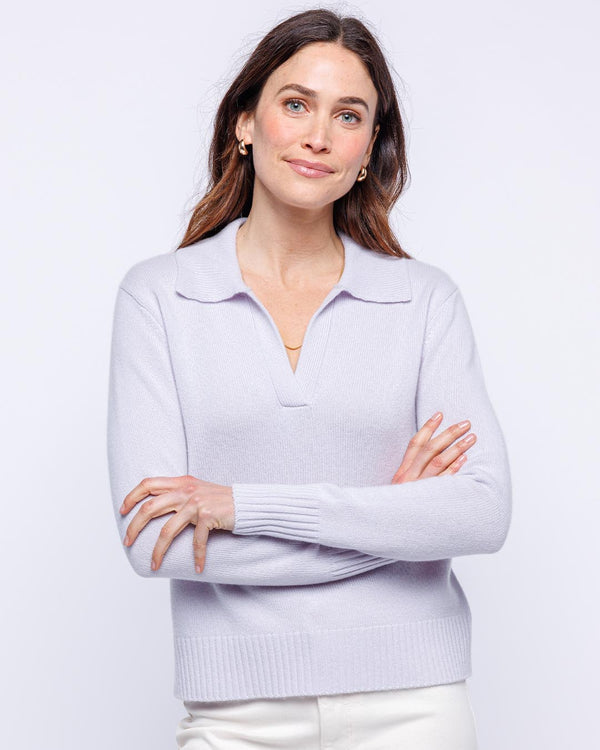 LIFESTYLE / EDITORIAL: Woman wearing lilac cashmere polo sweater with collar, standing with arms crossed against white