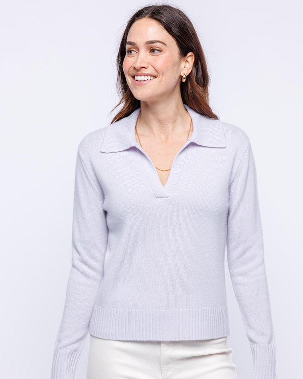 LIFESTYLE / EDITORIAL: Woman smiling wearing lilac cashmere polo sweater with collar and white pants against white background