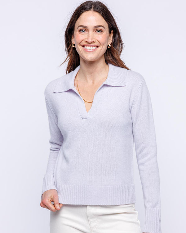 LIFESTYLE / EDITORIAL: Woman wearing lilac cashmere polo crew sweater and white pants, smiling against white background