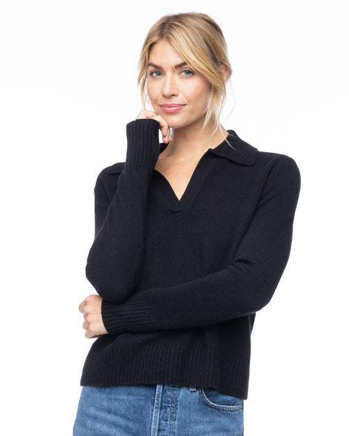 Three-quarter view image of a woman wearing a black V-neck cashmere polo sweater with blue jeans against white background