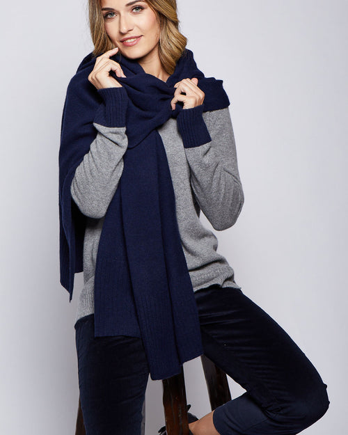 LIFESTYLE / EDITORIAL: Woman seated wearing grey cashmere sweater and navy ribbed cashmere travel wrap scarf