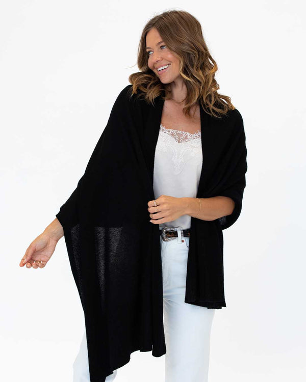 LIFESTYLE / EDITORIAL: Woman smiling wearing a black cashmere wrap over white lace top and white pants against white