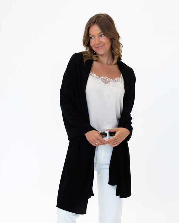 LIFESTYLE / EDITORIAL: Woman wearing black cashmere wrap over white lace-trim camisole and white pants, standing against