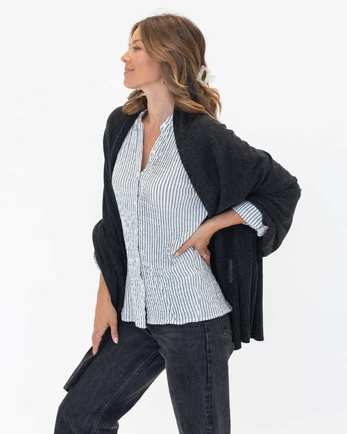 LIFESTYLE / EDITORIAL: Woman wearing charcoal cashmere wrap over striped shirt and black jeans, standing in profile against