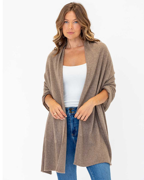 LIFESTYLE / EDITORIAL: Woman wearing a driftwood-colored cashmere travel wrap over white top and blue jeans against white