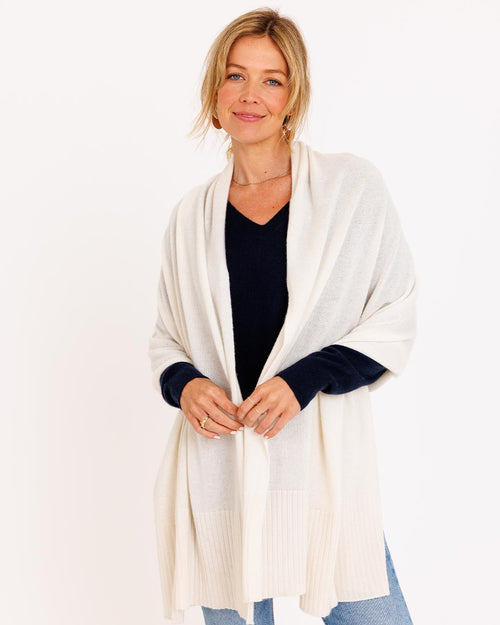 LIFESTYLE / EDITORIAL: Woman wearing ivory cashmere travel wrap over navy sweater and jeans, standing against white