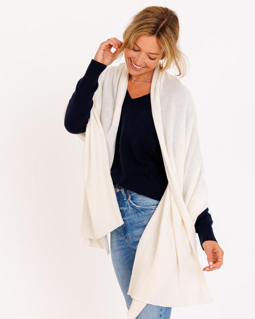 LIFESTYLE / EDITORIAL: Woman wearing ivory cashmere wrap over navy sweater and jeans, smiling and looking down
