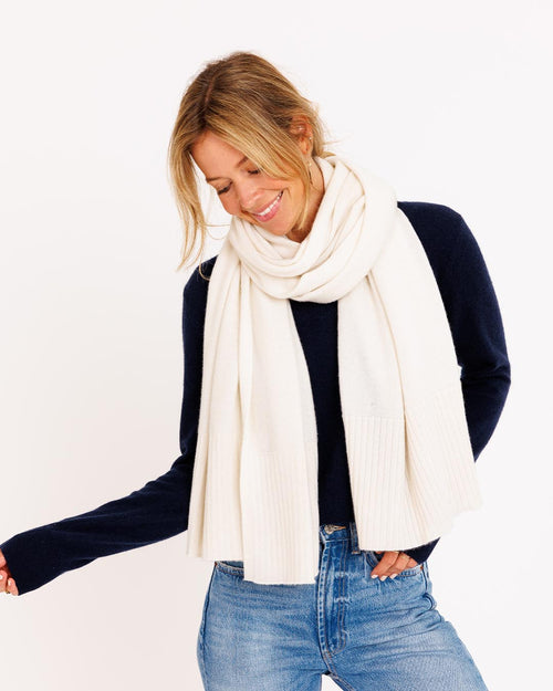 Three-quarter view image of a woman wearing an ivory cashmere travel wrap scarf with navy sweater and blue jeans