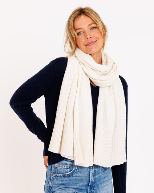 LIFESTYLE / EDITORIAL: Woman wearing ivory cashmere travel wrap scarf and navy sweater with blue jeans against white