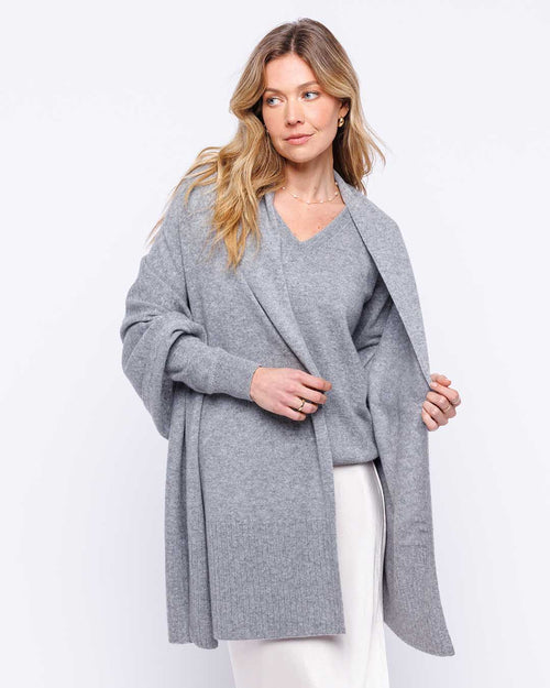 Woman wearing light gray cashmere wrap and sweater with white pants against white background