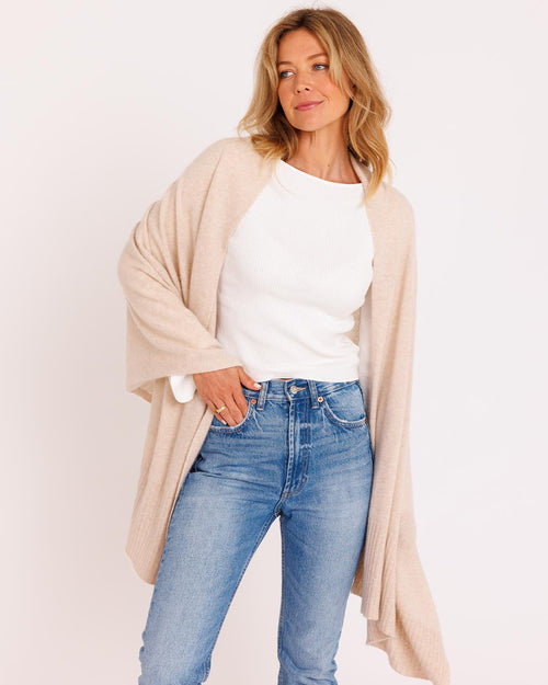 LIFESTYLE / EDITORIAL: Woman wearing oatmeal cashmere wrap over white top and blue jeans against plain background