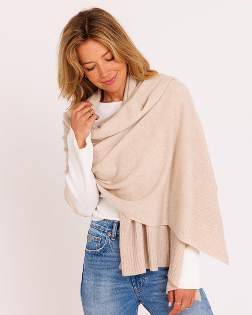 LIFESTYLE / EDITORIAL: Woman wearing oatmeal cashmere travel wrap over white top and blue jeans, smiling with eyes closed