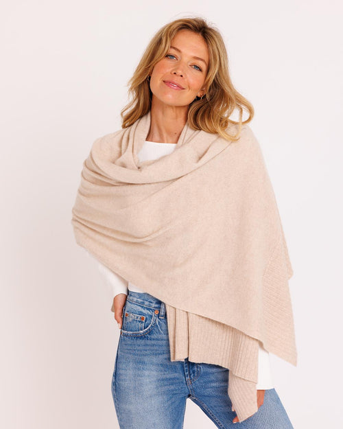 Three-quarter view image of a woman wearing an oatmeal cashmere travel wrap over a white top and blue jeans