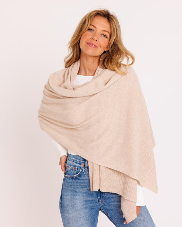Three-quarter view image of a woman wearing an oatmeal cashmere travel wrap over a white top and blue jeans