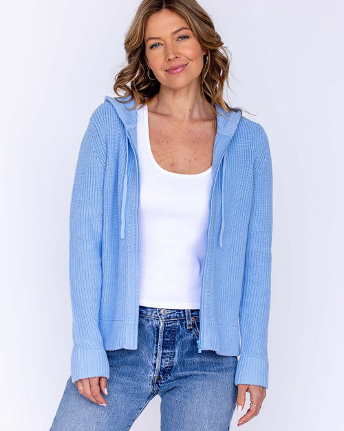LIFESTYLE / EDITORIAL: Woman wearing light blue cotton hoodie, white tank top, and blue jeans against white background