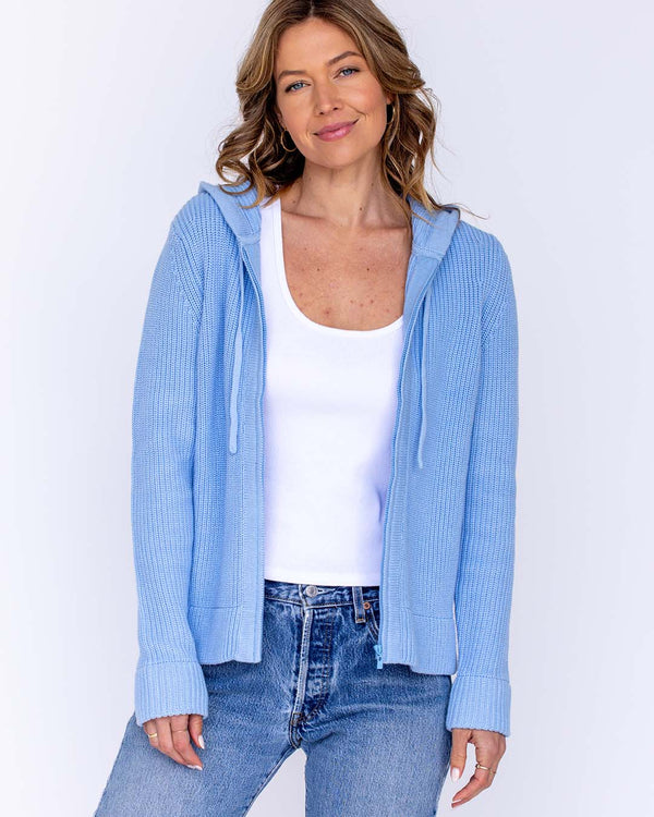 LIFESTYLE / EDITORIAL: Woman wearing light blue cotton hoodie, white tank top, and blue jeans against white background