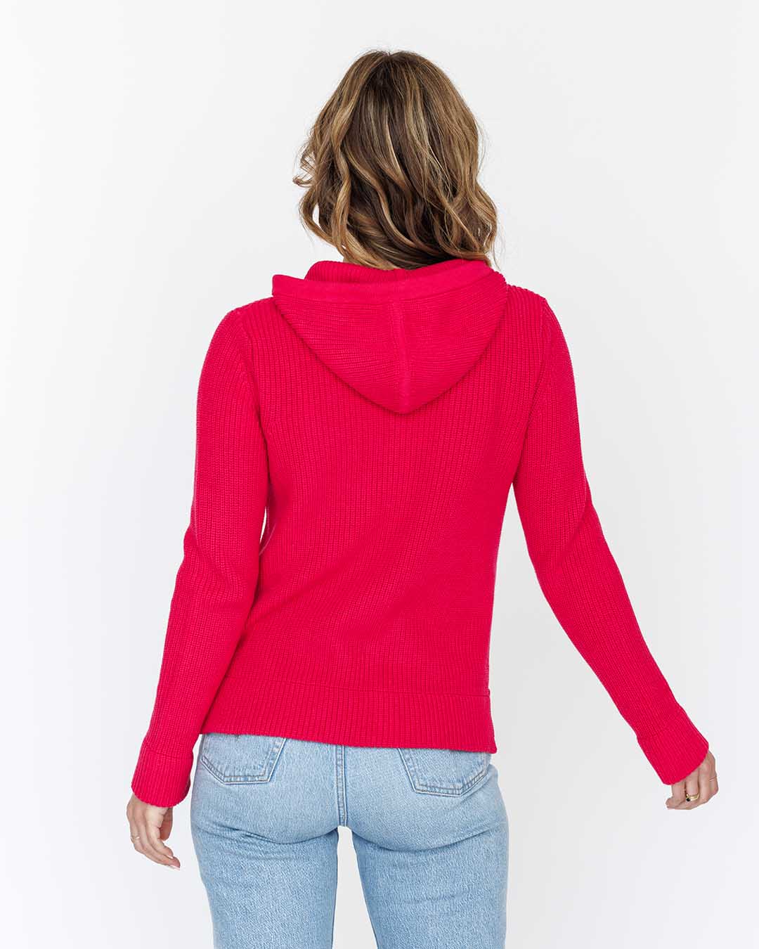 Woman wearing bright pink cotton fisherman hoodie and light blue jeans, back view against white background