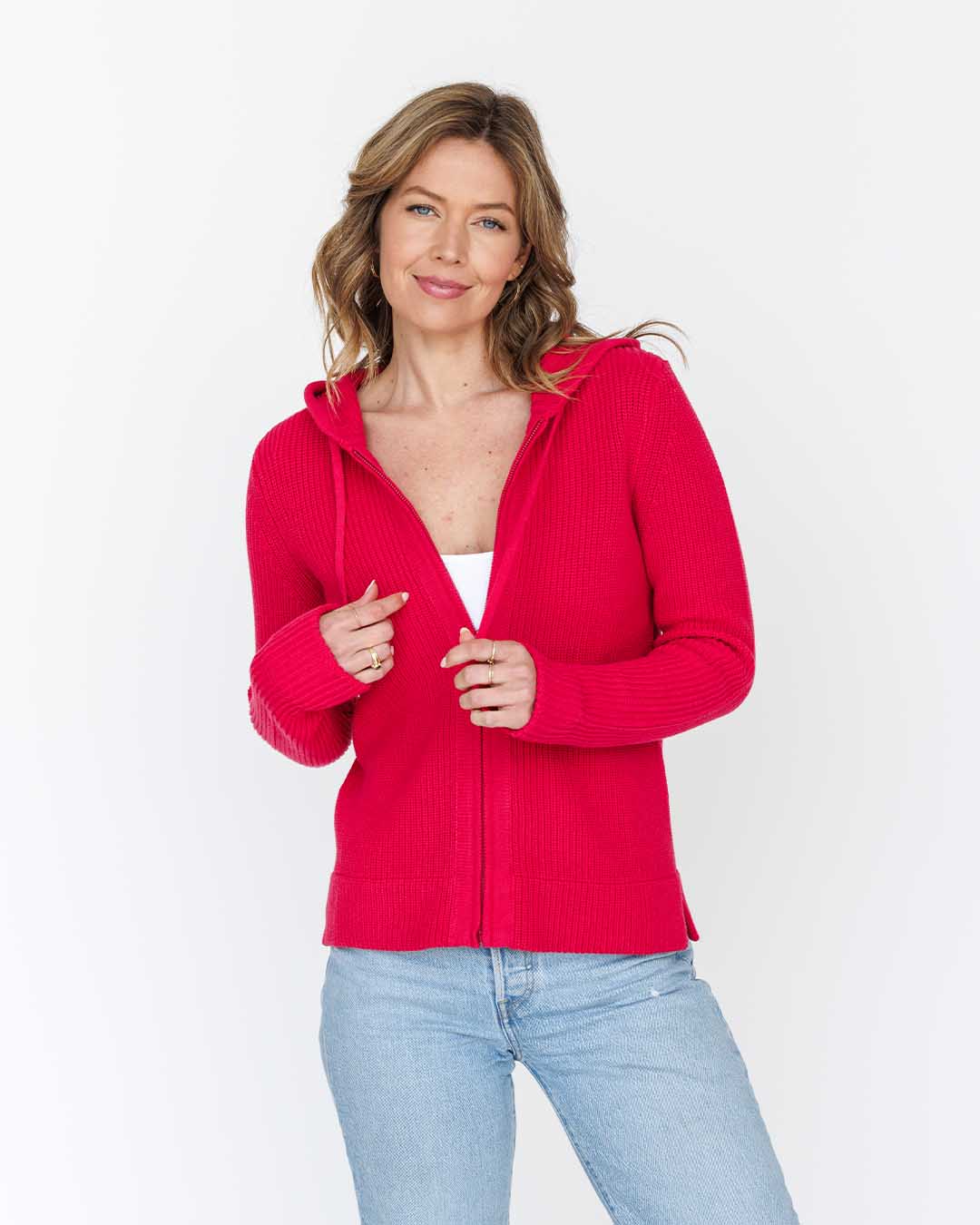 LIFESTYLE / EDITORIAL: Woman wearing bright red zip-up hoodie and light blue jeans against white background