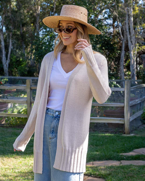 LIFESTYLE / EDITORIAL: Woman outdoors wearing oatmeal cotton open cardigan, white V-neck shirt, jeans, straw hat, and