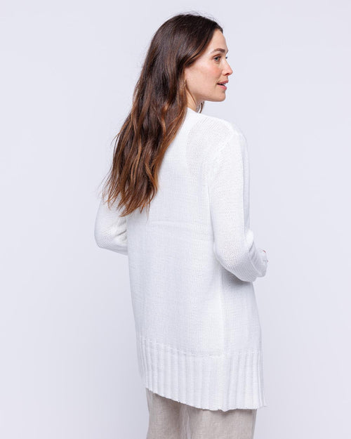 Woman wearing long white open cotton cardigan, shown from back, against plain light background