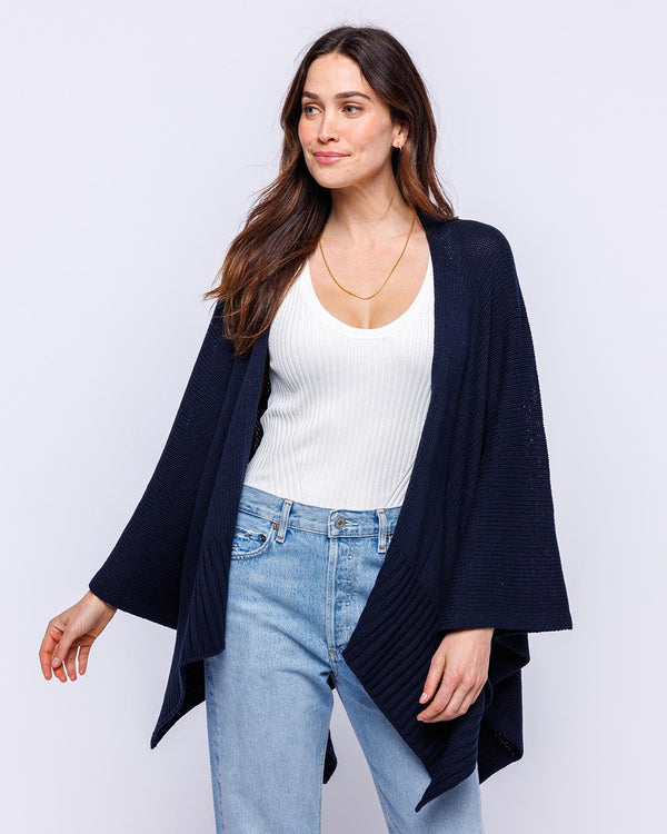 LIFESTYLE / EDITORIAL: Woman wearing navy cotton serape, white ribbed tank top, and light blue jeans against white background