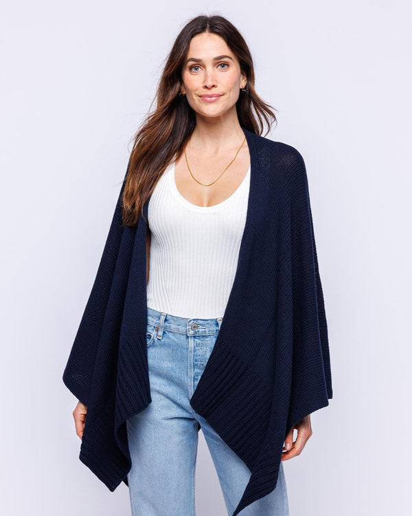 LIFESTYLE / EDITORIAL: Woman wearing navy cotton serape over white ribbed tank and light blue jeans against white background
