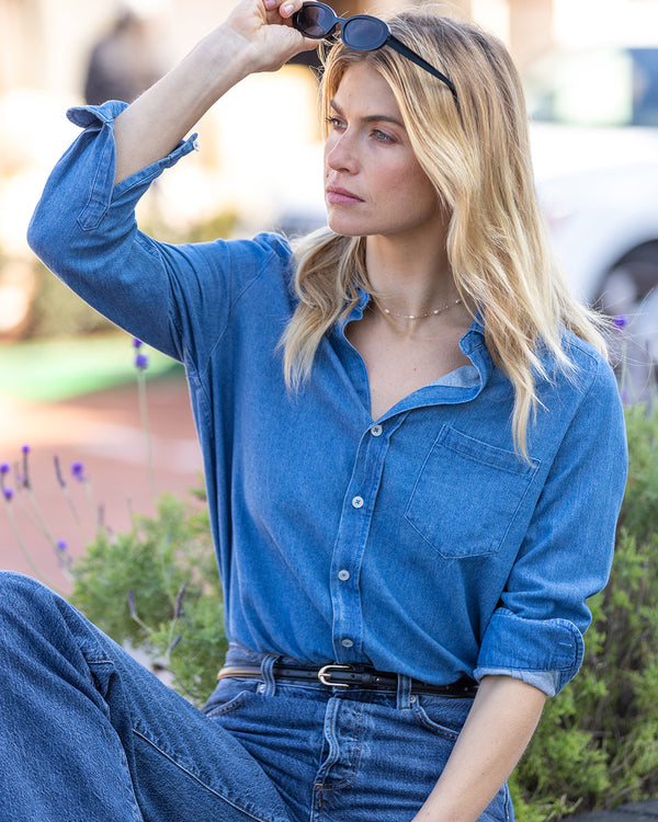 LIFESTYLE / EDITORIAL: Woman in medium wash denim button-up shirt and jeans, adjusting sunglasses outdoors