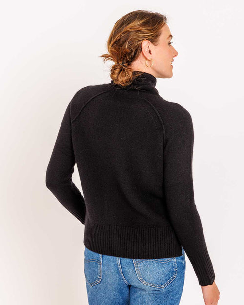 LIFESTYLE / EDITORIAL: Woman wearing black cashmere turtleneck sweater and blue jeans, facing away against white background